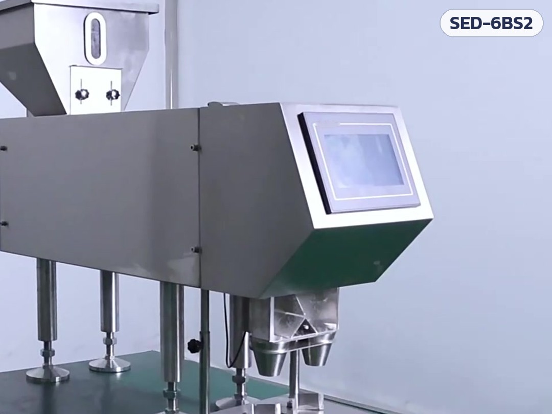 เครื่องนับเม็ดยา/แคปซูลกึ่งอัตโนมัติ 6 ช่อง 2 หัวลงขวด SED-6BS2 – ภาพเครื่องจริงมุมเฉียง: ถังพักวัตถุดิบ ช่องมองระดับ จอสัมผัส และกรวยทางออก 2 หัวด้านหน้า (ภาพจากคลิปเครื่องจริง)